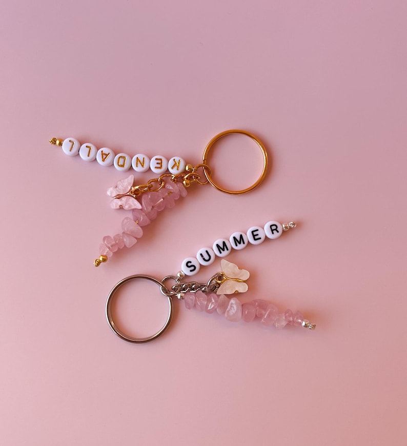 May include: Two pink and gold keychains with pink crystal beads and white butterfly charms. One keychain spells "KENDAL" and the other spells "SUMMER".