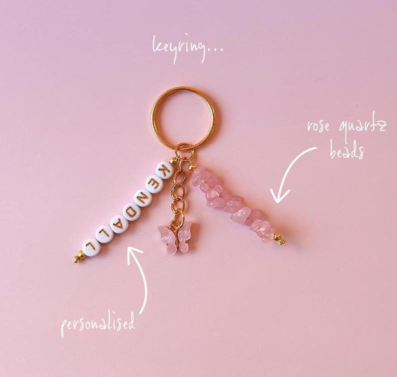 May include: A gold keychain with a personalized name "KENDALL" spelled out in white beads, a pink butterfly charm, and a strand of rose quartz beads.
