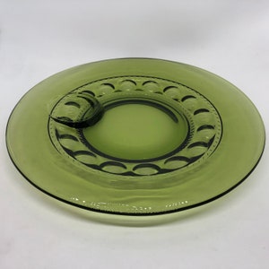 Op de afbeelding: Een groene glazen serveerschaal met een verhoogde rand en een kleinere, ronde schaal in het midden. De schaal heeft een decoratief patroon van kleine cirkels rond de rand.