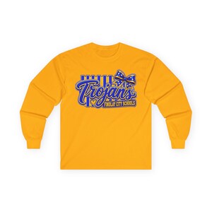 May include: A gold long-sleeve shirt featuring a blue graphic with vertical stripes, a polka-dot bow, and the text "Trojans" above "FINDLAY CITY SCHOOLS" with a small heart icon. The design is centered on the chest of the crew neck garment.