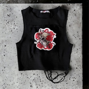 Puede incluir: Top corto negro sin mangas con un parche gráfico de calavera y rosas rojas. El top tiene un detalle de encaje en la parte inferior.