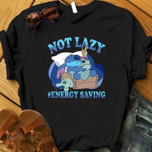 Pode incluir: Camiseta preta com um personagem de desenho animado azul segurando um brinquedo de pelúcia. O texto "NOT LAZY #ENERGY SAVING" está impresso na camiseta.