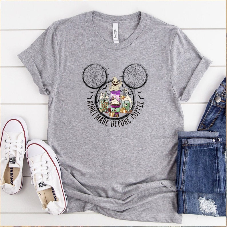May include: A gray t-shirt with a Mickey Mouse silhouette featuring a spiderweb design and the text "Nightmare Before Coffee". The design includes a ghost, a pumpkin, and coffee cups.