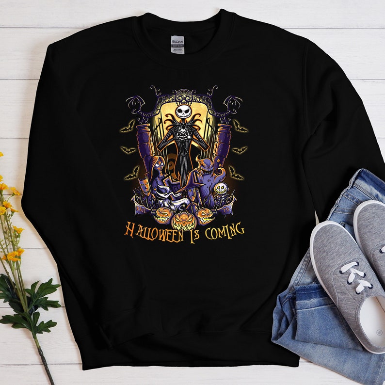 May include: Black sweatshirt with a graphic print of Jack Skellington from The Nightmare Before Christmas. The graphic features Jack Skellington, Sally, and Oogie Boogie. The text "HALLOWEEN IS COMING" is printed below the graphic.