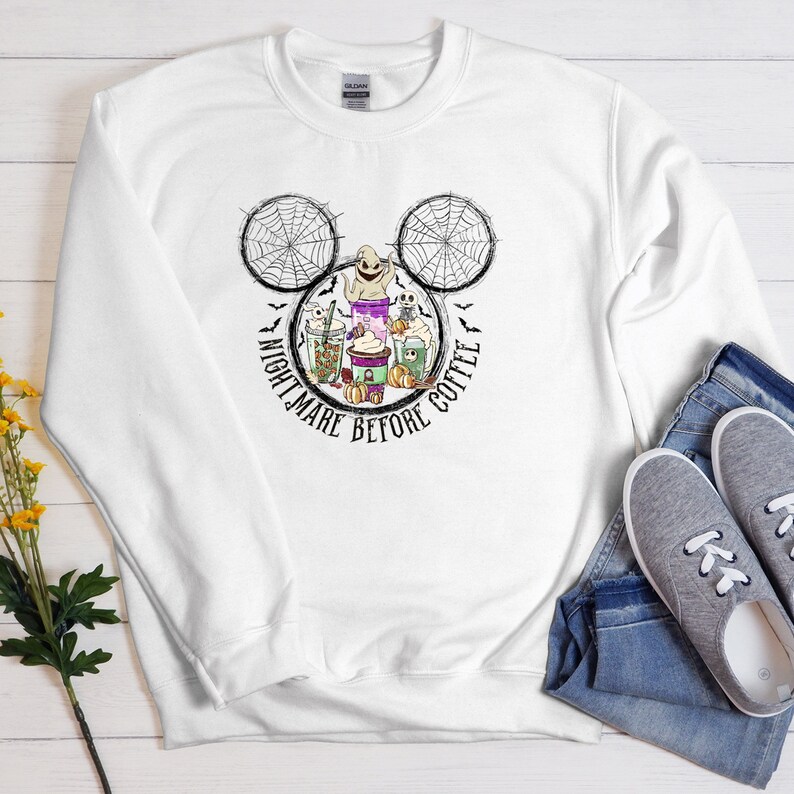 May include: White sweatshirt with a black and white Mickey Mouse head design featuring a ghost, spiderwebs, and coffee cups. The text "Nightmare Before Coffee" is written around the Mickey Mouse head.