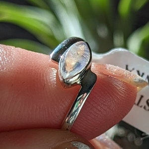 May include: A silver ring with a moonstone set in an oval shape. The ring is on a finger and the text on the tag reads "BF M'ST SRI LANKA".