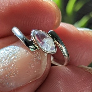 May include: A silver ring featuring a clear, iridescent gemstone set in a zig-zag design.