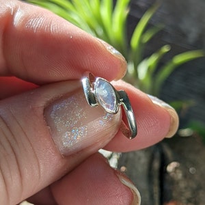 May include: A silver ring featuring a white moonstone set in a curved design.