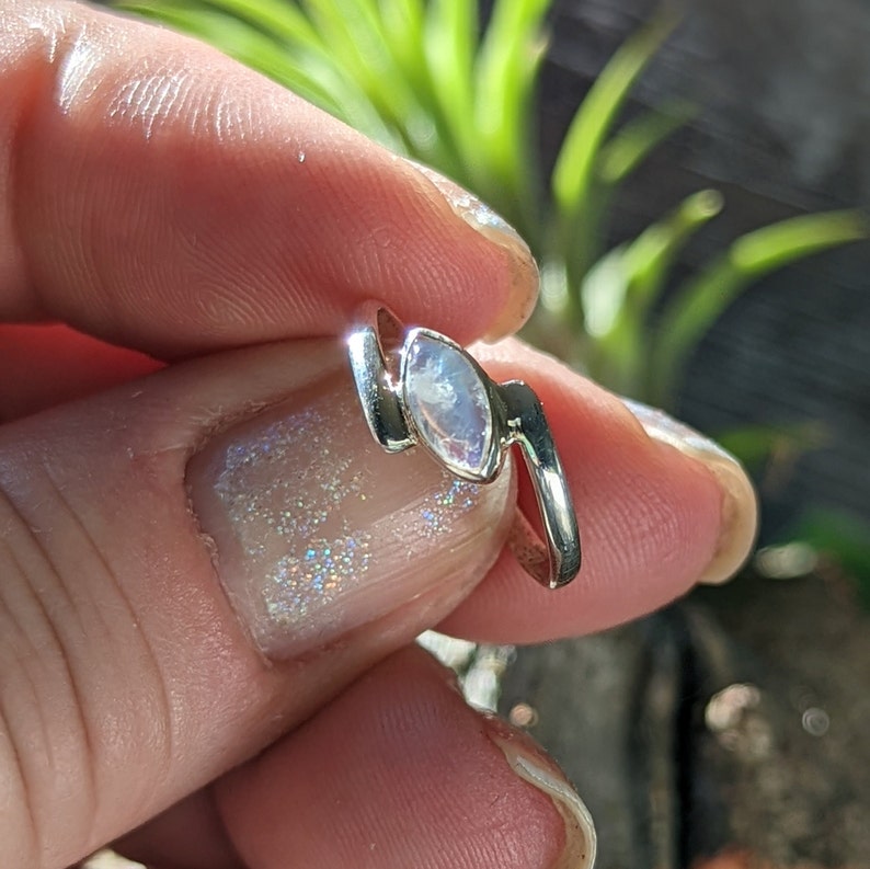 May include: A silver ring featuring a white moonstone set in a curved design.