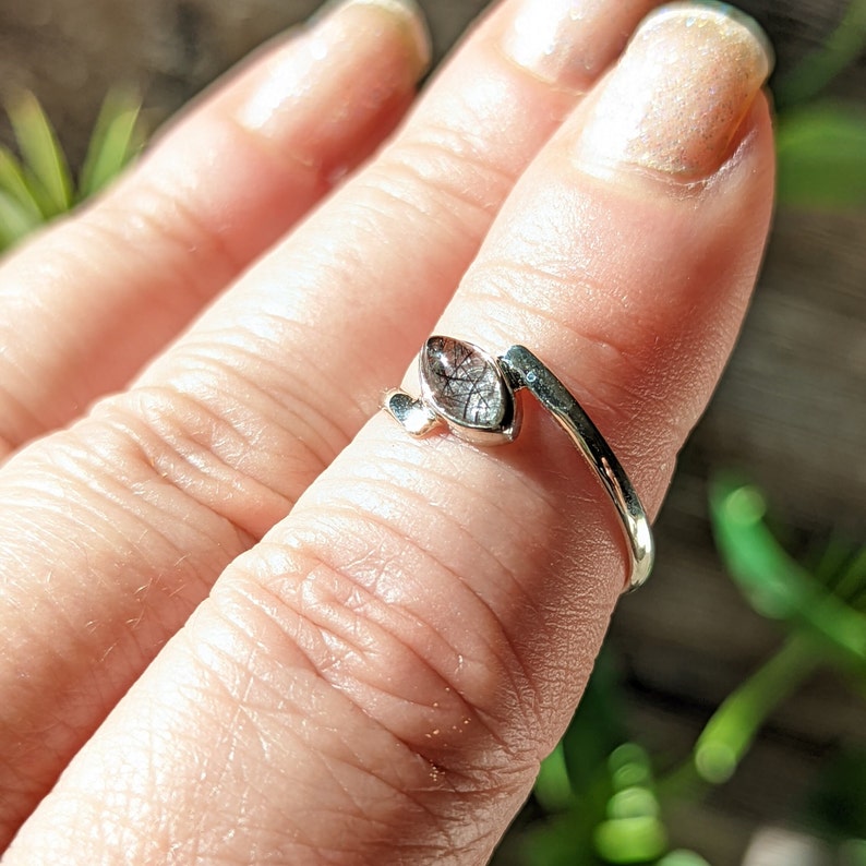 Op de afbeelding: Een zilveren ring met een heldere, gefacetteerde edelsteen. De ring is ontworpen om om de vinger te wikkelen.