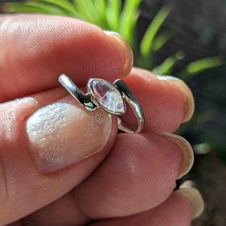 May include: A silver ring featuring a clear iridescent gemstone set in a zig-zag design.