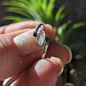 May include: A silver ring with a clear, faceted gemstone set in a curved band.