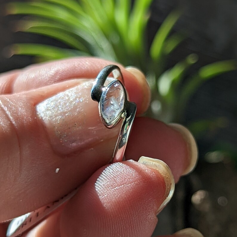 May include: A silver ring with a clear, faceted gemstone set in a curved band.