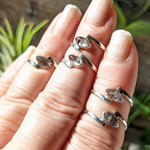 Op de afbeelding: Vier zilveren ringen met heldere kwartsstenen. De ringen zijn ontworpen met een gebogen band en een marquise-vormige steen.