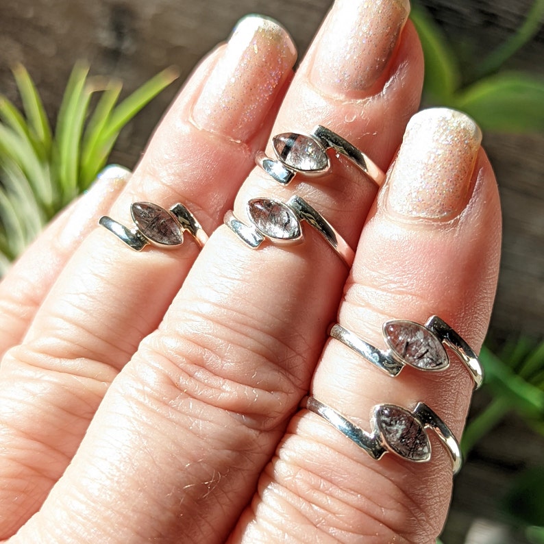 Op de afbeelding: Vier zilveren ringen met heldere kwartsstenen. De ringen zijn ontworpen met een gebogen band en een marquise-vormige steen.