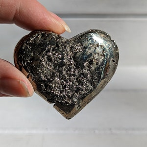 May include: A heart-shaped pyrite crystal with a rough, textured surface. The crystal is a dark gray color with a metallic sheen.