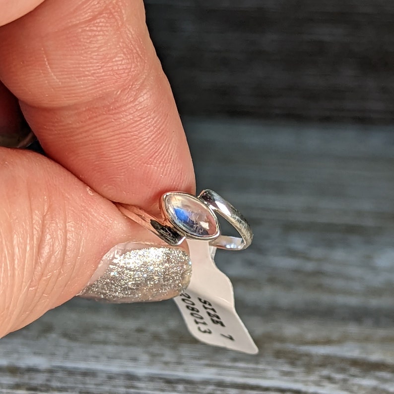 May include: A silver ring with a clear moonstone set in a curved band. The ring is size 7 and is shown on a finger.