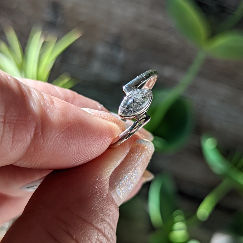 Op de afbeelding: Een zilveren ring met een heldere, marquise-vormige edelsteen met zwarte insluitsels. De ring is gezet op een zilveren band.