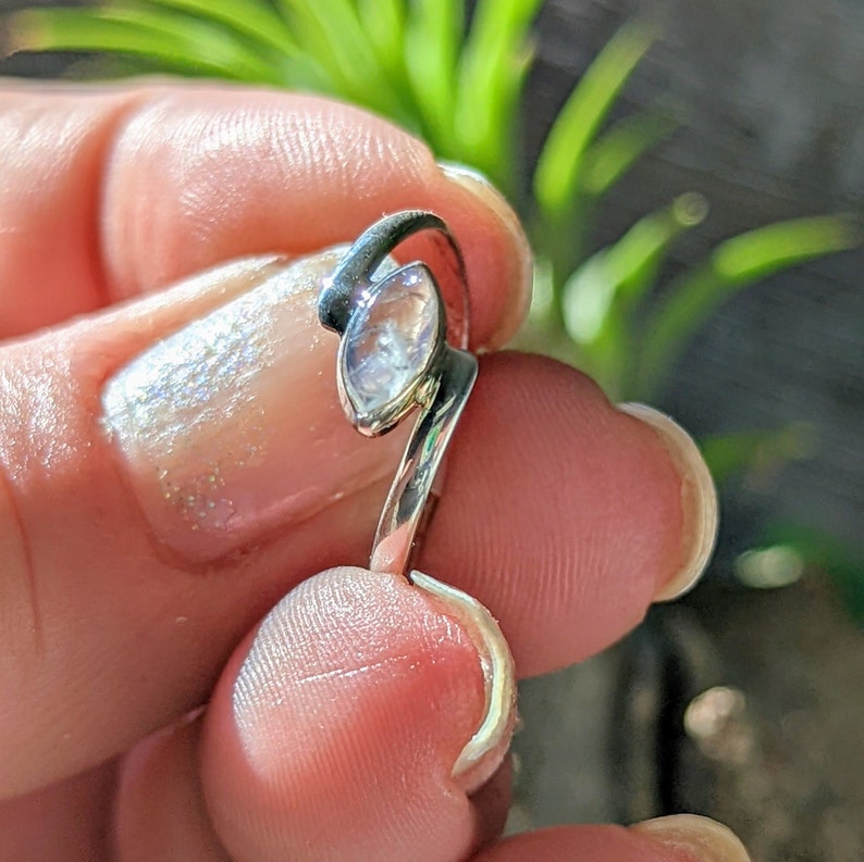 May include: A silver ring featuring a clear, faceted gemstone set in a leaf-shaped design.