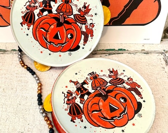 May include: Two vintage Halloween tambourines. Each tambourine features a smiling orange pumpkin with a black face, surrounded by costumed figures. The tambourines have a red rim and a light green background with scattered stars.