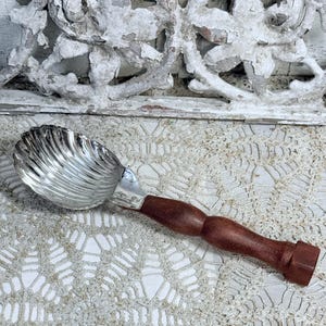 May include: A vintage ice cream scoop. The scoop is silver-coloured with a ridged design, and the handle is made of dark brown wood. The scoop has a classic design. The handle is a rich, dark brown colour.