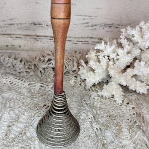 May include: A vintage egg beater with a wooden handle and a metal coil whisk. The handle is a light brown color, and the whisk is made of silver-colored metal. The egg beater is a kitchen utensil.