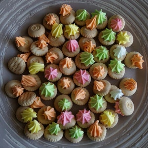 May include: A plate of small, round cookies with colorful frosting. The cookies are arranged in a circular pattern and are a variety of colors, including pink, green, yellow, orange, and white.