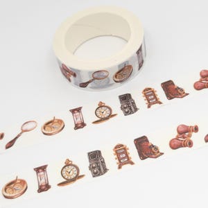 May include: A roll of washi tape with a white background and brown, gold, and white illustrations of vintage items, including a compass, magnifying glass, hourglass, clock, camera, binoculars, and a number dial.