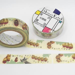 May include: A roll of washi tape with a light yellow background and a green and brown pattern of acorns and squirrels. The tape is labeled "宮沢賢治" and "15mm x 10m巻" in Japanese. The tape is designed by Shinzi Katoh.
