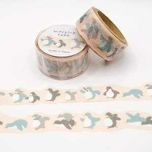 May include: Masking tape rolls with a penguin pattern. The tape features penguins in various poses, in shades of blue, gray, and black, on a light pink background. One roll is unraveled, showing the repeating penguin design. The packaging says "masking tape" and "made in Japan."