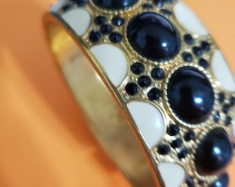 May include: A gold bangle bracelet with black and white enamel accents. The bracelet is decorated with round black stones and white enamel accents.