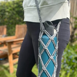 May include: A gray crocheted water bottle holder with a teal water bottle inside. The holder is worn as a crossbody bag.
