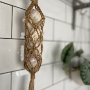 Könnte beinhalten: Nahaufnahme eines braunen, geflochtenen Knoblauchhalters, der an einem Holzring hängt. Der Halter ist mit weißen Knoblauchzehen gefüllt.