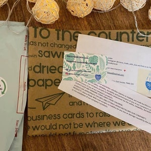 May include: A brown paper package with the text "To the counter" printed on it. The package is wrapped with a blue and white envelope with the text "REUSED PACKAGING" printed on it. The package is surrounded by string lights.