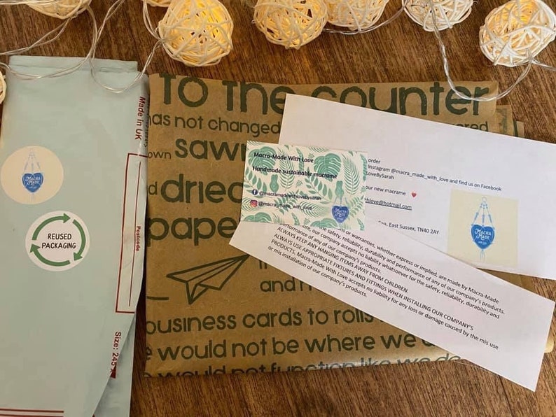 May include: A brown paper package with the text "To the counter" printed on it. The package is wrapped with a blue and white envelope with the text "REUSED PACKAGING" printed on it. The package is surrounded by string lights.