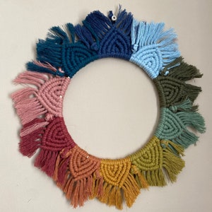 Puede incluir: Un tapiz de macram&eacute; de pared colorido con forma circular y detalles de flecos. El tapiz presenta un arco&iacute;ris de colores, incluyendo rosa, rojo, naranja, amarillo, verde, azul y morado.