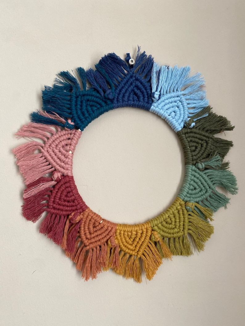 Puede incluir: Un tapiz de macram&eacute; de pared colorido con forma circular y detalles de flecos. El tapiz presenta un arco&iacute;ris de colores, incluyendo rosa, rojo, naranja, amarillo, verde, azul y morado.