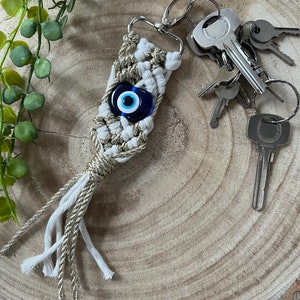 May include: White and gold macrame keychain with a blue evil eye charm attached to a silver key ring with multiple keys.