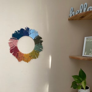 Puede incluir: Un tapiz de macram&eacute; de arco&iacute;ris colorido con forma circular y detalles de flecos. El tapiz est&aacute; hecho con diferentes tonos de hilo rosa, naranja, amarillo, verde, azul y morado.