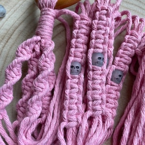 Pode incluir: Um suporte de plantas de macramé rosa com um anel de madeira no topo e contas em forma de caveira.