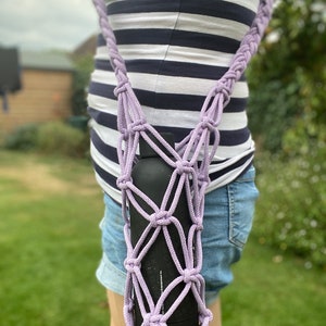May include: A purple crocheted bottle holder with a black water bottle inside. The holder is worn as a crossbody bag.