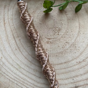 May include: A gold-colored pen with a braided rope design. The pen is lying on a wooden surface.