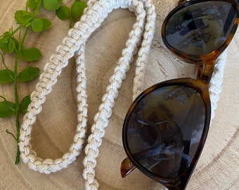 May include: A white crocheted eyeglass strap with a tortoiseshell pair of sunglasses on a wooden surface.