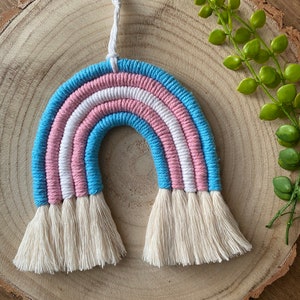 May include: A handmade rainbow wall hanging made with blue, pink and white yarn. The rainbow has a white tassel at the bottom.