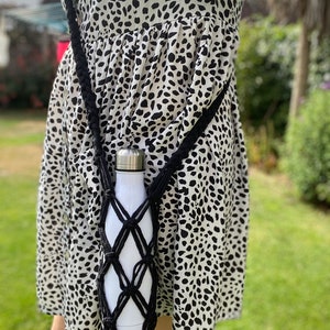 May include: A black crocheted water bottle holder with a white water bottle inside. The holder is worn as a crossbody bag.