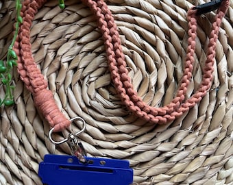 Puede incluir: Un cordón trenzado de color coral con un porta credenciales de plástico azul y un clip de metal plateado.