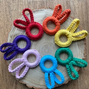 Könnte beinhalten: Sieben gehäkelte Hasenringe in einem Regenbogen von Farben, die in einem Kreis auf einer Holzoberfläche angeordnet sind.