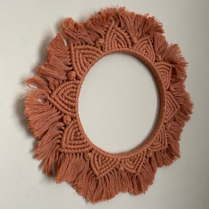 May include: A large, round macrame wall hanging with a fringe border. The macrame is made with a light brown cord and has a geometric pattern.