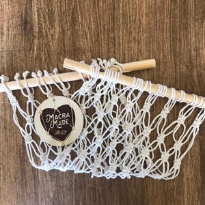 A white macrame hammock with two wooden dowels, laid out on a flat wooden surface.