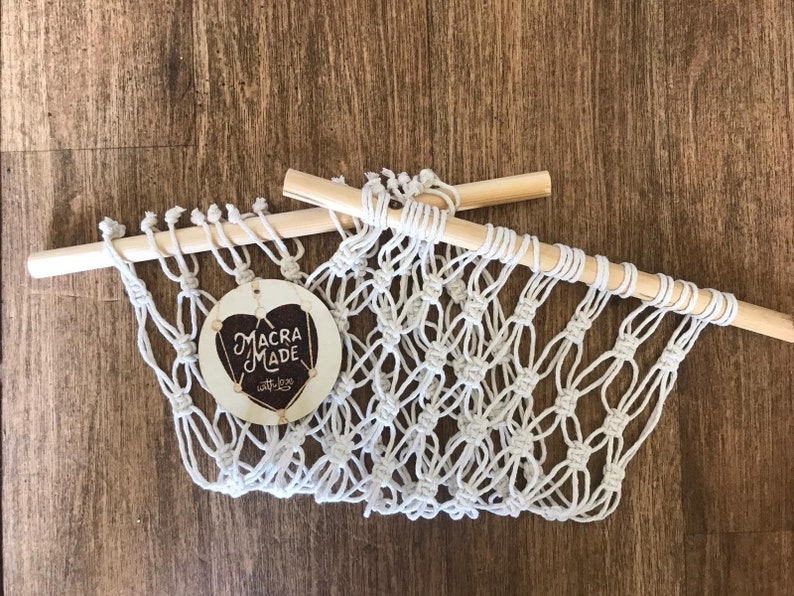 A white macrame hammock with two wooden dowels, laid out on a flat wooden surface.